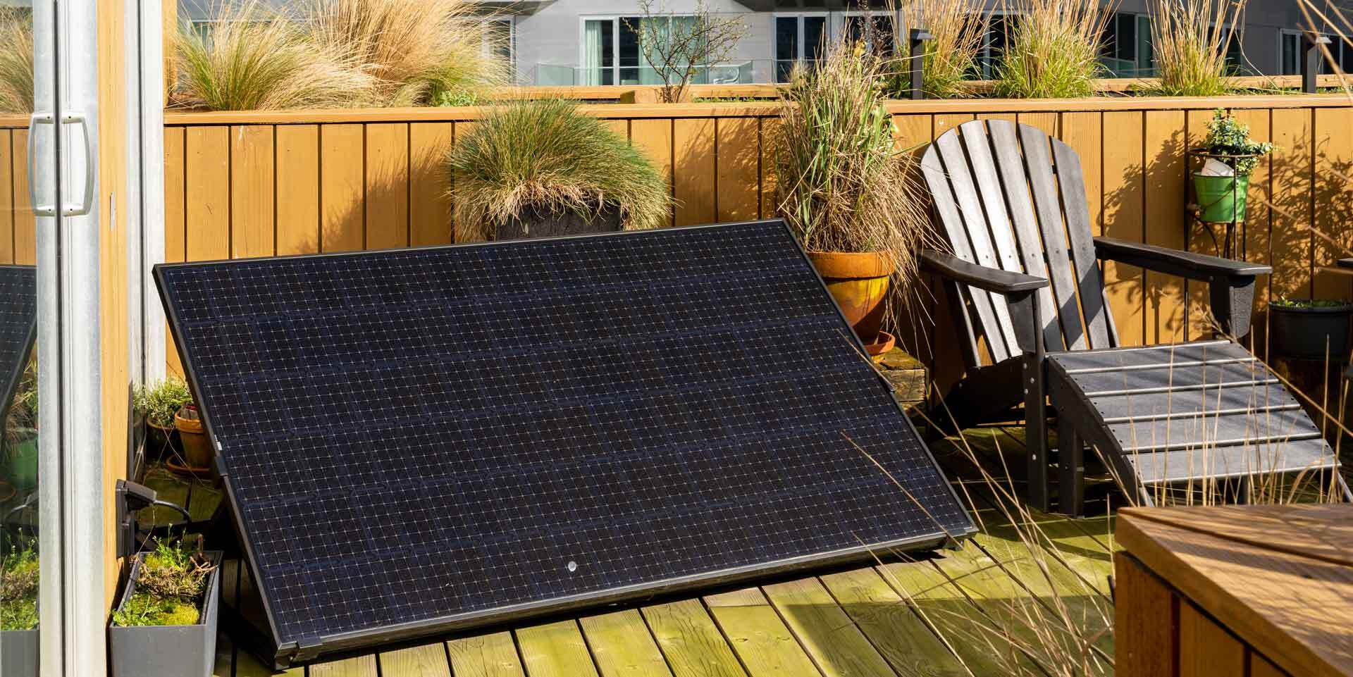 Solarmodul als Balkonkraftwerk auf einer Dachterrasse mit Sonnenstuhl und Bepflanzung im Hintergrund