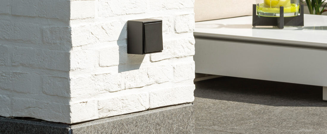 Aufbausteckdose in schwarz von JUNG montiert an einer weißen Mauerwand