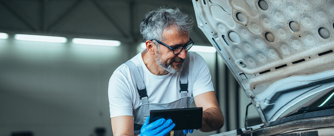 Handwerker über einer Motorhaube gelehnt mit Leuchten im Hintergrund von Lichttechnik Pracht - ECO Line