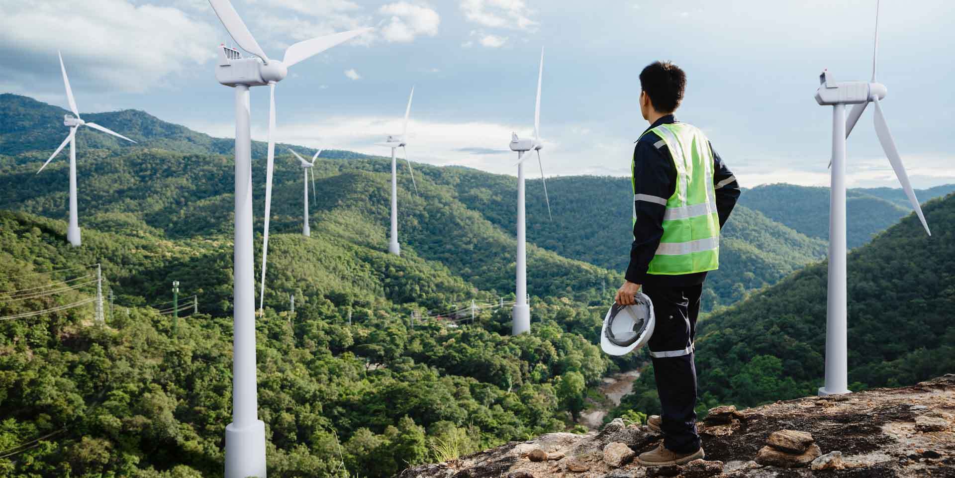 Arbeiter steht auf Berg und Blickt auf Tal mit Windrädern